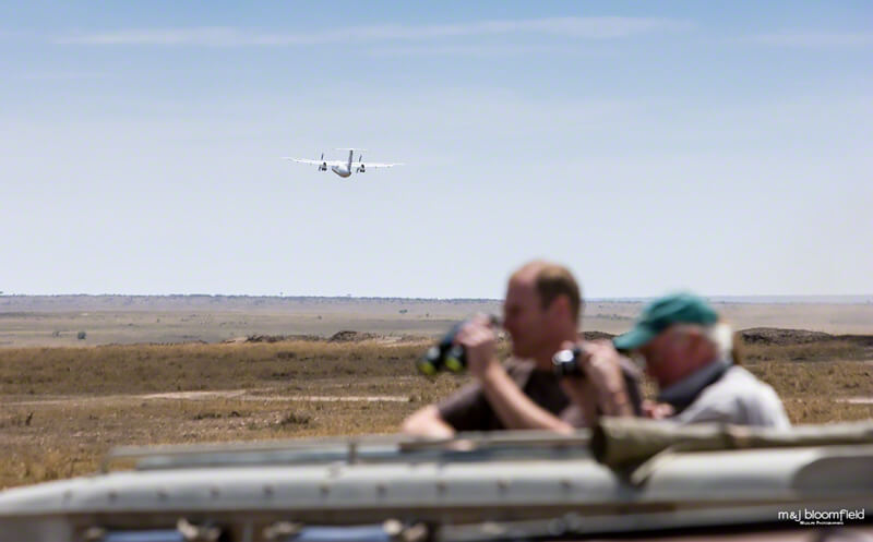 Tourists in a four by four safari vehicle watching game from the sunroof while a plane takes off from a bush air-strip in Kenya’s Masai Mara